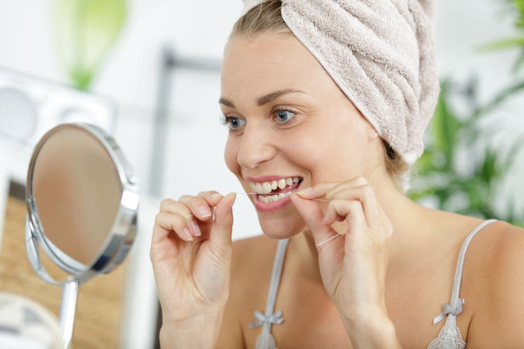 woman cleaning her teeth using dental floss